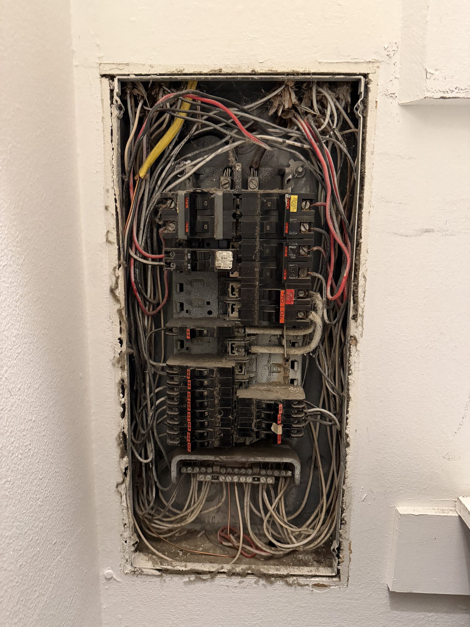 An older electrical panel with its cover off, showing dusty breakers and tangled wiring
