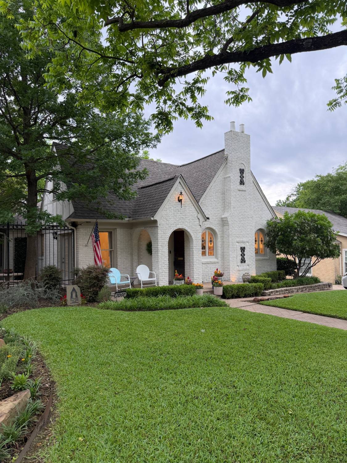 A white-brick Tudor cottage in Lakewood, with an arched entry and the porch lights on